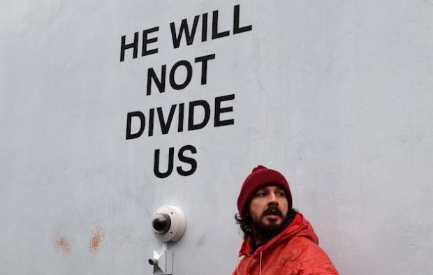 US actor Shia LaBeouf(L)is seen during his He Will Not Divide Us livestream outside the Museum of the Moving Image in Astoria, in the Queens borough of New York January 24, 2017 as a protest against President Donald Trump. LaBeouf has installed a camera at the Museum of the Moving Image in New York that will run a continuous live stream for the duration of Trumps presidency. LaBeouf is inviting the public to participate in the project by saying the phrase, He will not divide us, into the camera. / AFP / TIMOTHY A. CLARY        (Photo credit should read TIMOTHY A. CLARY/AFP/Getty Images) 