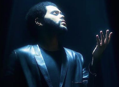 The Weeknd в тёмном жакете под синим светом поднимает руку